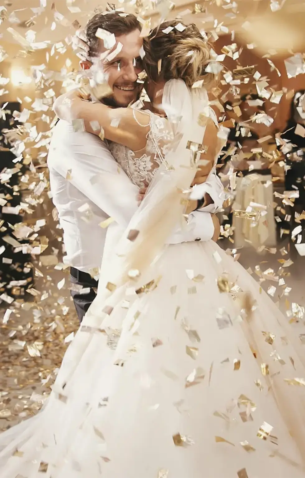 Hochzeitspaar umarmt sich lächelnd unter goldenem Konfetti.