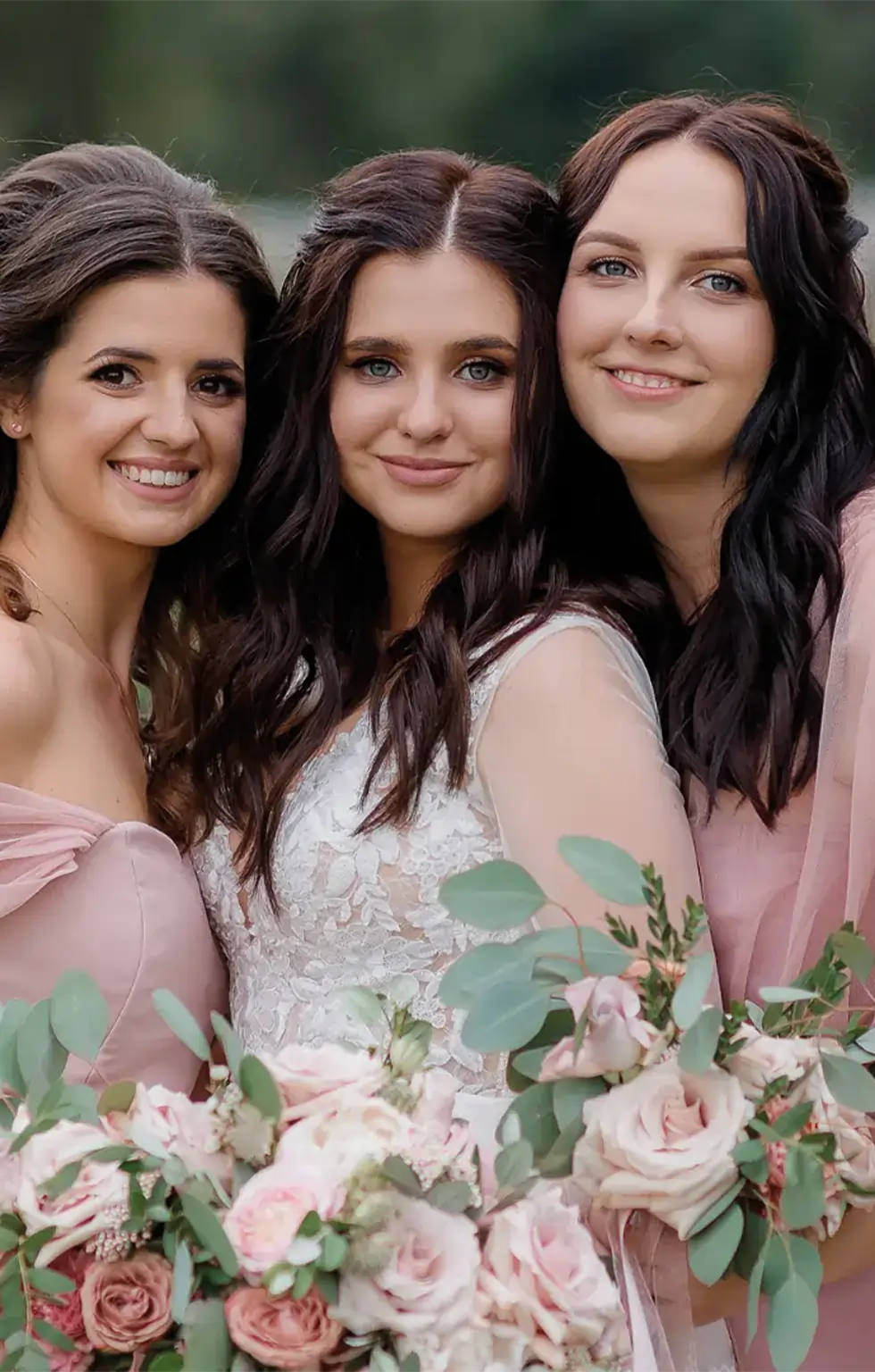 Drei Frauen in eleganter Kleidung mit Blumensträußen lächeln in die Kamera.
