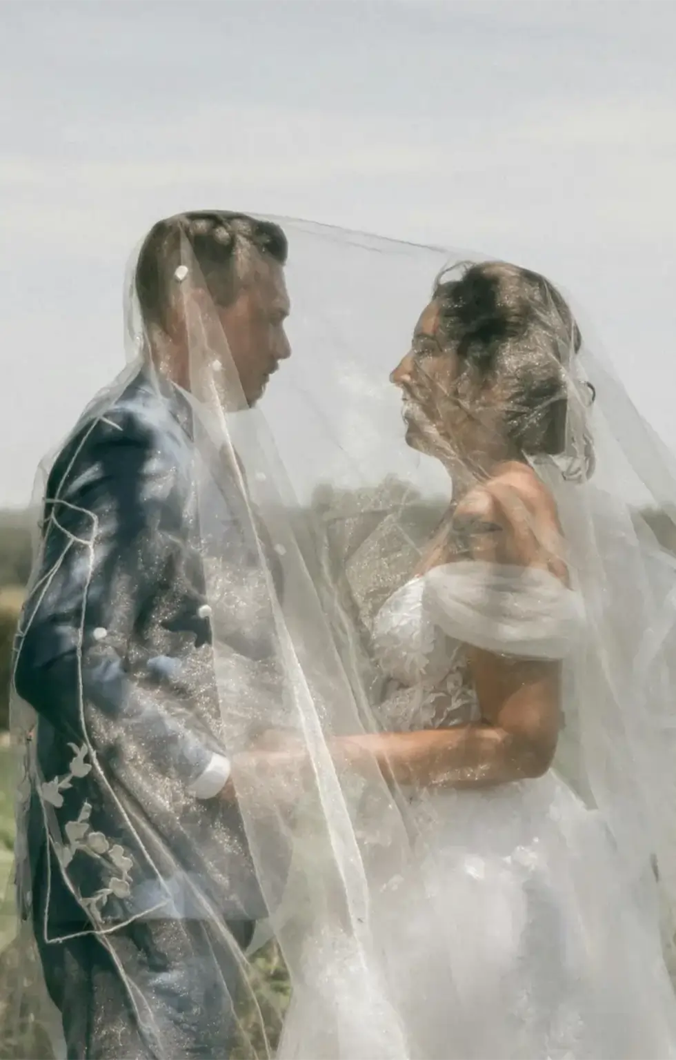 Ein Brautpaar steht unter einem transparenten Schleier im Freien.